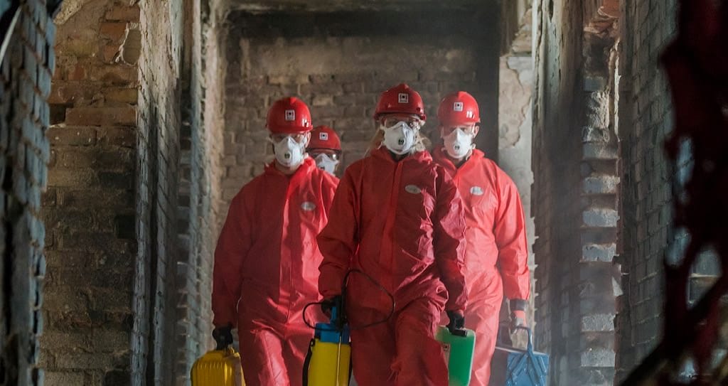 Dipendenti con tute DPI rosse che camminano in una struttura danneggiata