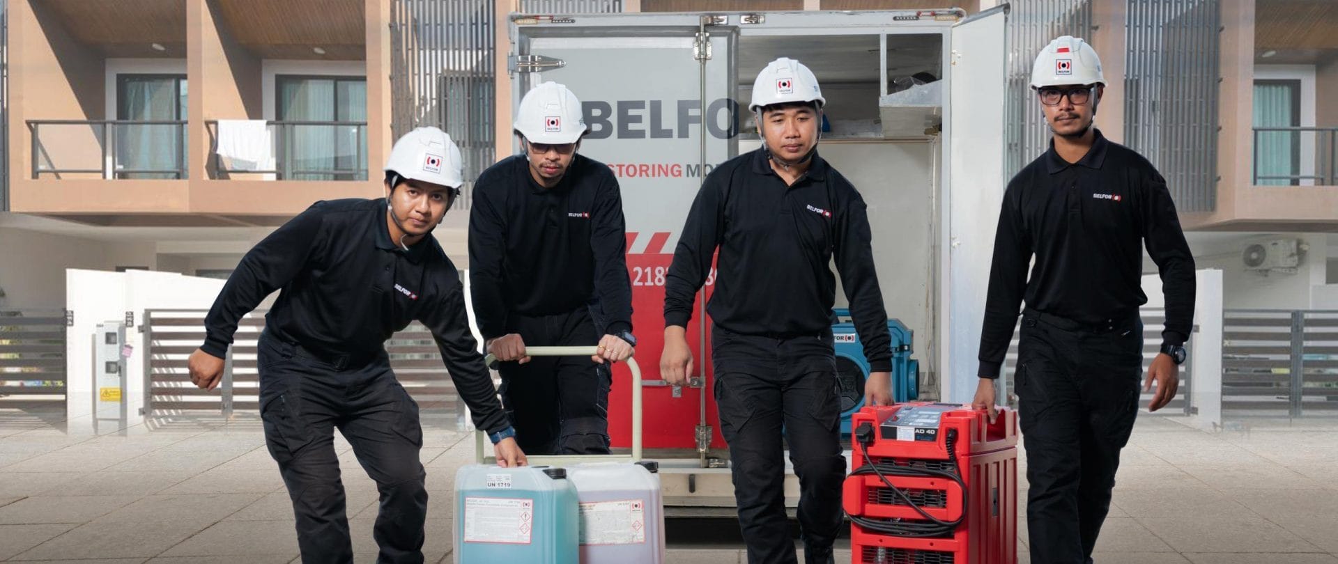 BELFOR employees carrying equipment with a trailer and a building in the background