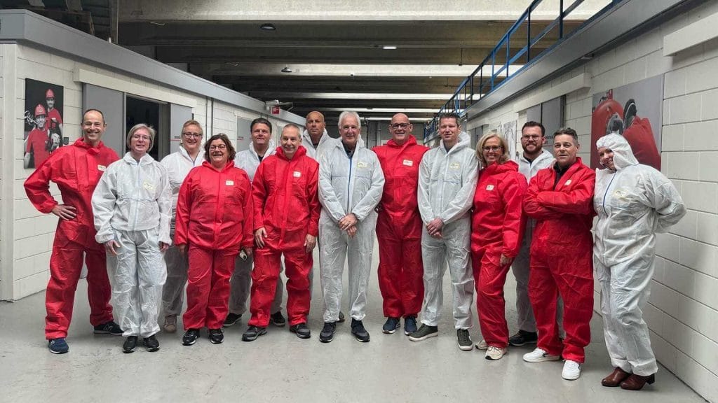 Groep medewerkers in beschermende pakken staat in een gang