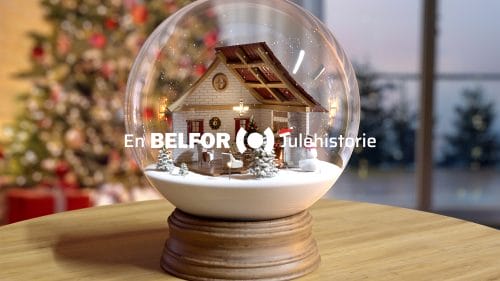 En snøkule på et trebord, med et pyntet juletre i bakgrunnen. På bildet står det «En BELFOR Julehistorie».