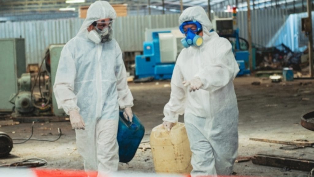 Two individuals in protective suits walking through a factory.