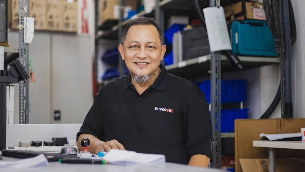 BELFOR staff sits at a desk in a storage or maintenance room surrounded by office supplies and equipment