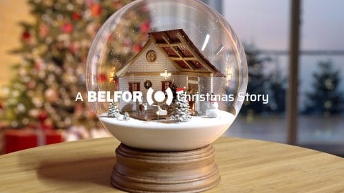 Snow globe on a wooden table, with a decorated Christmas tree visible in the background. The image features the words ‘A BELFOR Christmas story’.