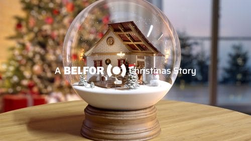 A snow globe on a wooden table, in the background is a decorated christmas tree and the slogan "A BELFOR Christmas Story" in front